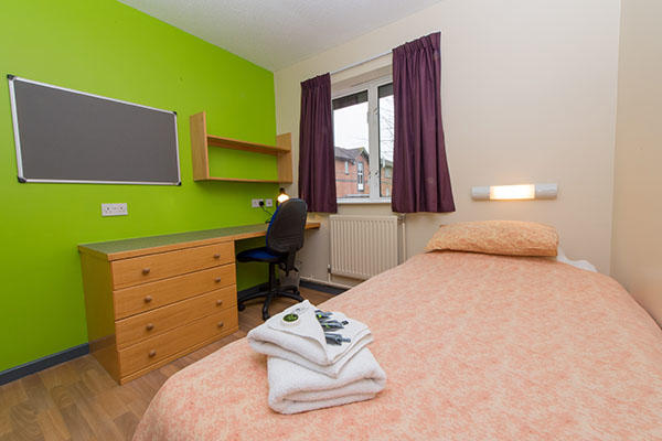 A bedroom inside ӶƵ accommodation. There is a single bed, a large pin board, desk, chest of drawers and a window in the room.